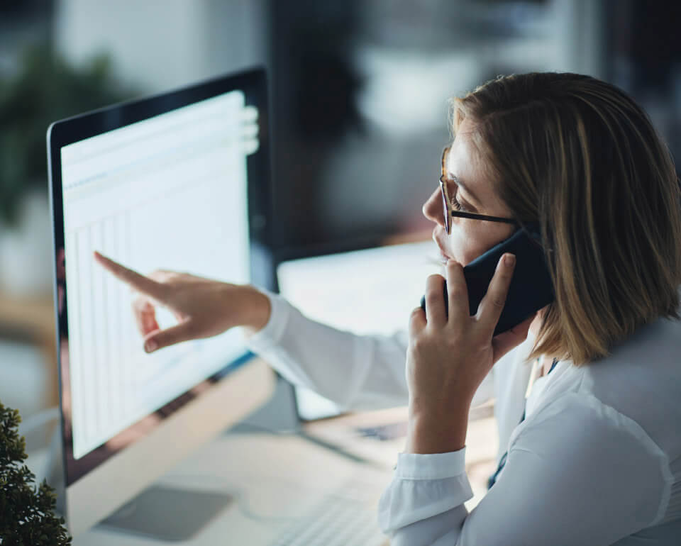 Caladis-Dienstplanerstellung-mobil Frau telefoniert während sie Daten auf dem Monitor betrachtet
